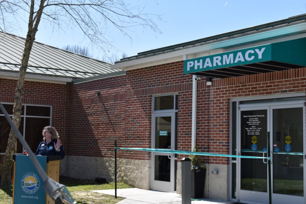 a woman standing at a podium in front of a pharmacy
