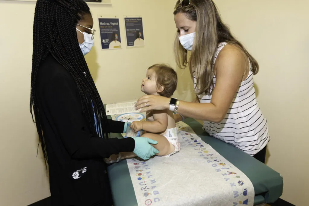 a woman in a face mask is giving a baby a bottle